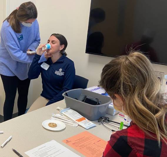 Student administering 3-Oz water test on a team member along with measuring the swallow duration using a stop watch and assessing hyolaryngeal function with a 4-finger test